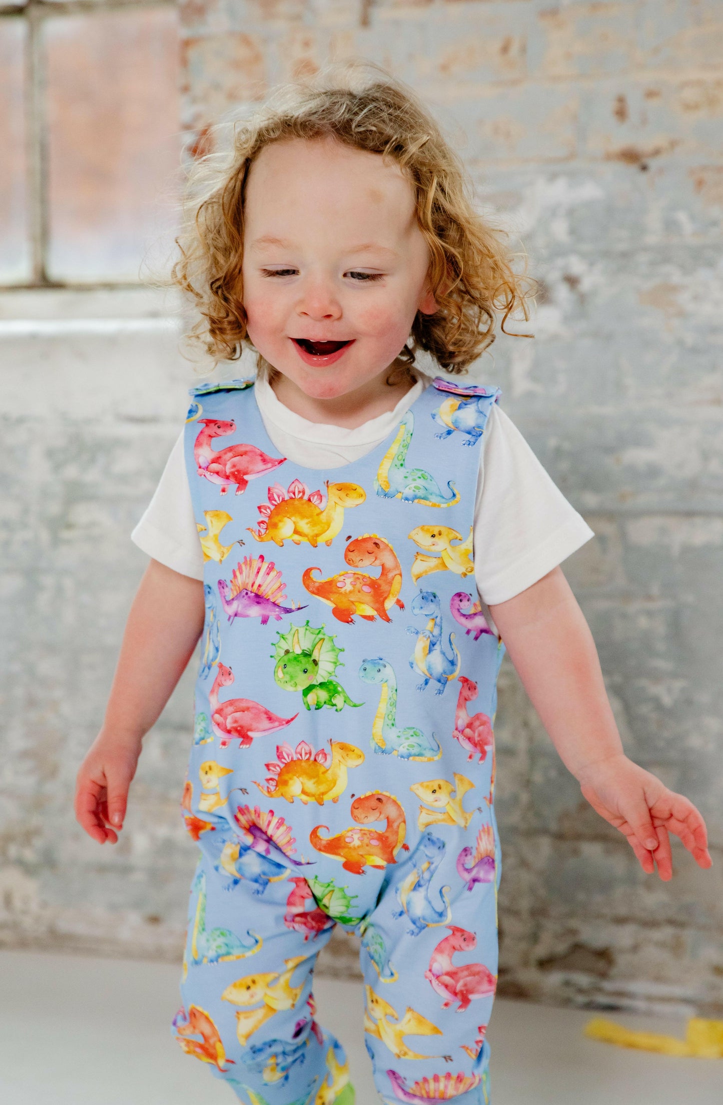 Blue cute dinosaur print romper handmade for babies and toddlers, fun for running, jumping and climbing. Dungarees style outfit in a stretchy cotton fabric handmade in Oxfordshire.