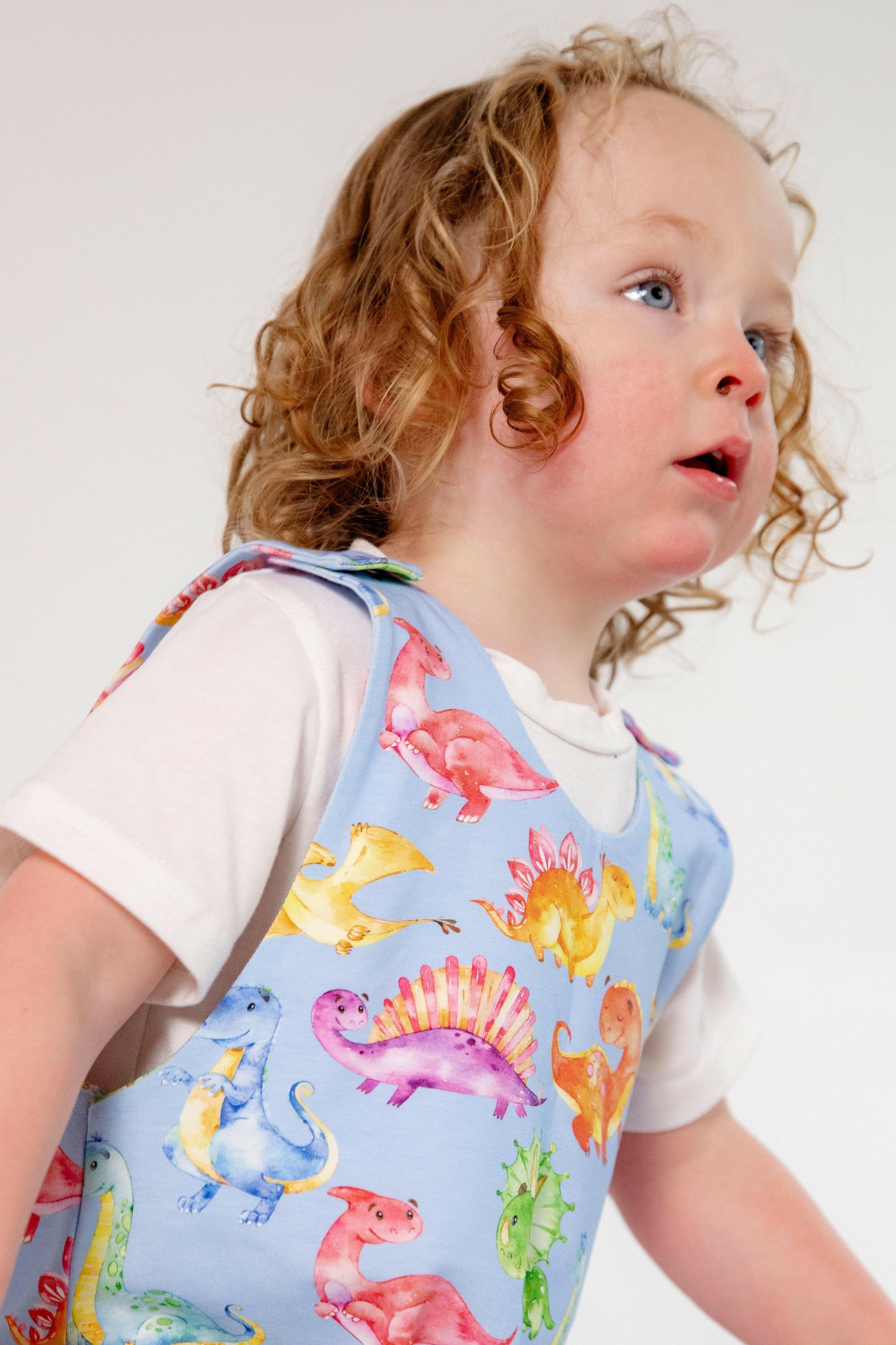 Blue cute dinosaur print romper handmade for babies and toddlers, fun for running, jumping and climbing. Dungarees style outfit in a stretchy cotton fabric handmade in Oxfordshire.