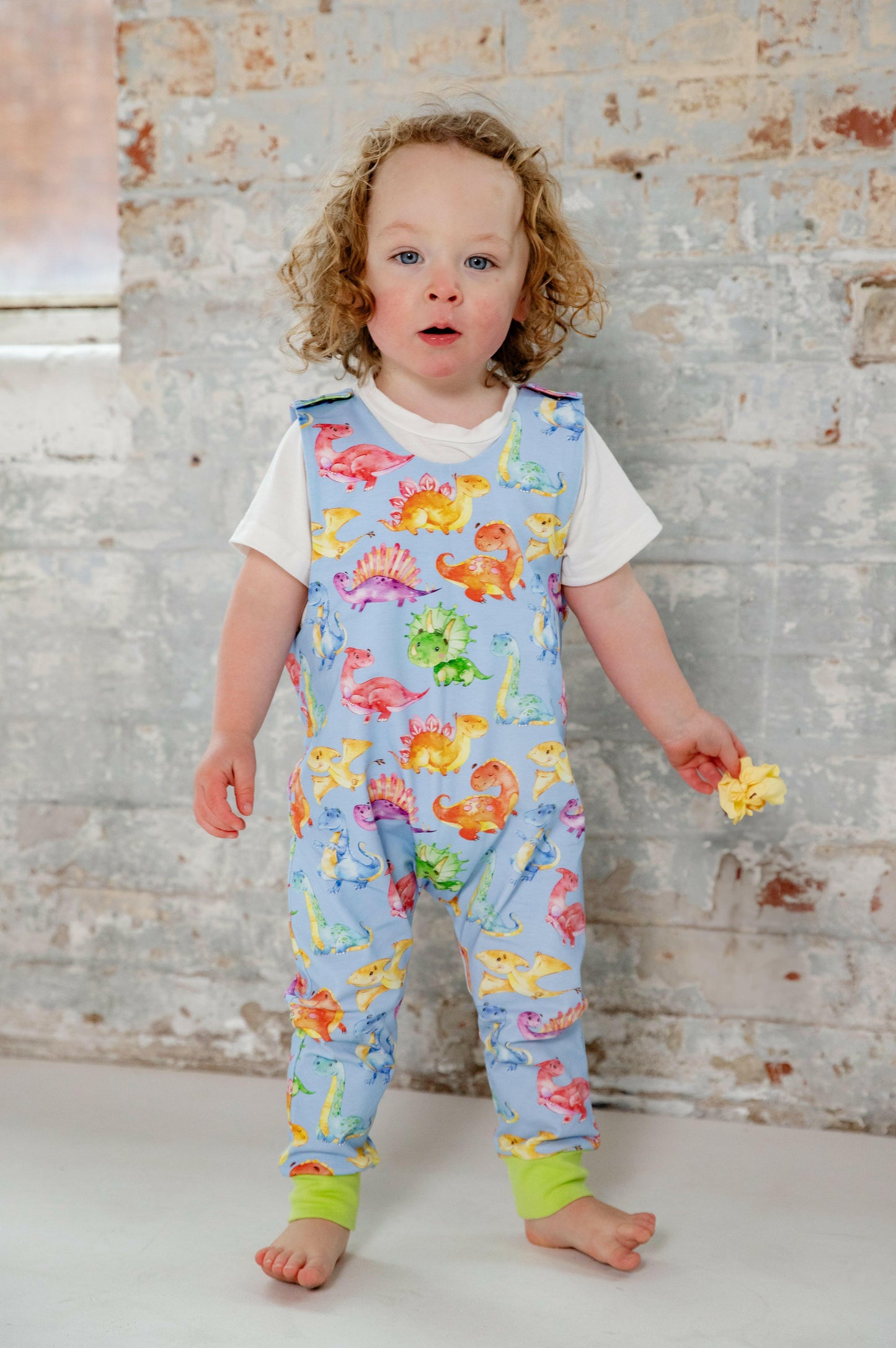 Blue cute dinosaur print romper handmade for babies and toddlers, fun for running, jumping and climbing. Dungarees style outfit in a stretchy cotton fabric handmade in Oxfordshire.