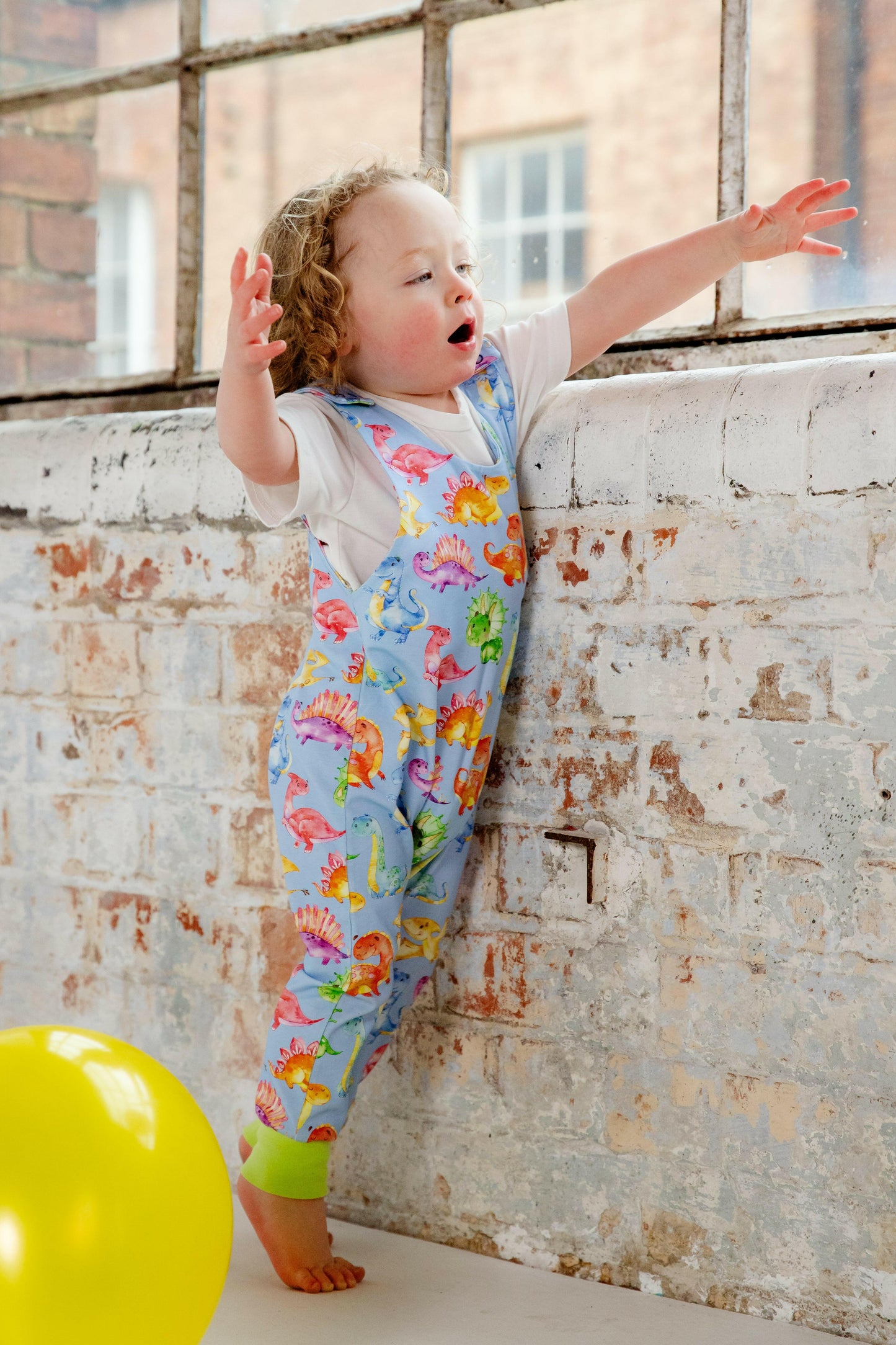 Blue cute dinosaur print romper handmade for babies and toddlers, fun for running, jumping and climbing. Dungarees style outfit in a stretchy cotton fabric handmade in Oxfordshire.