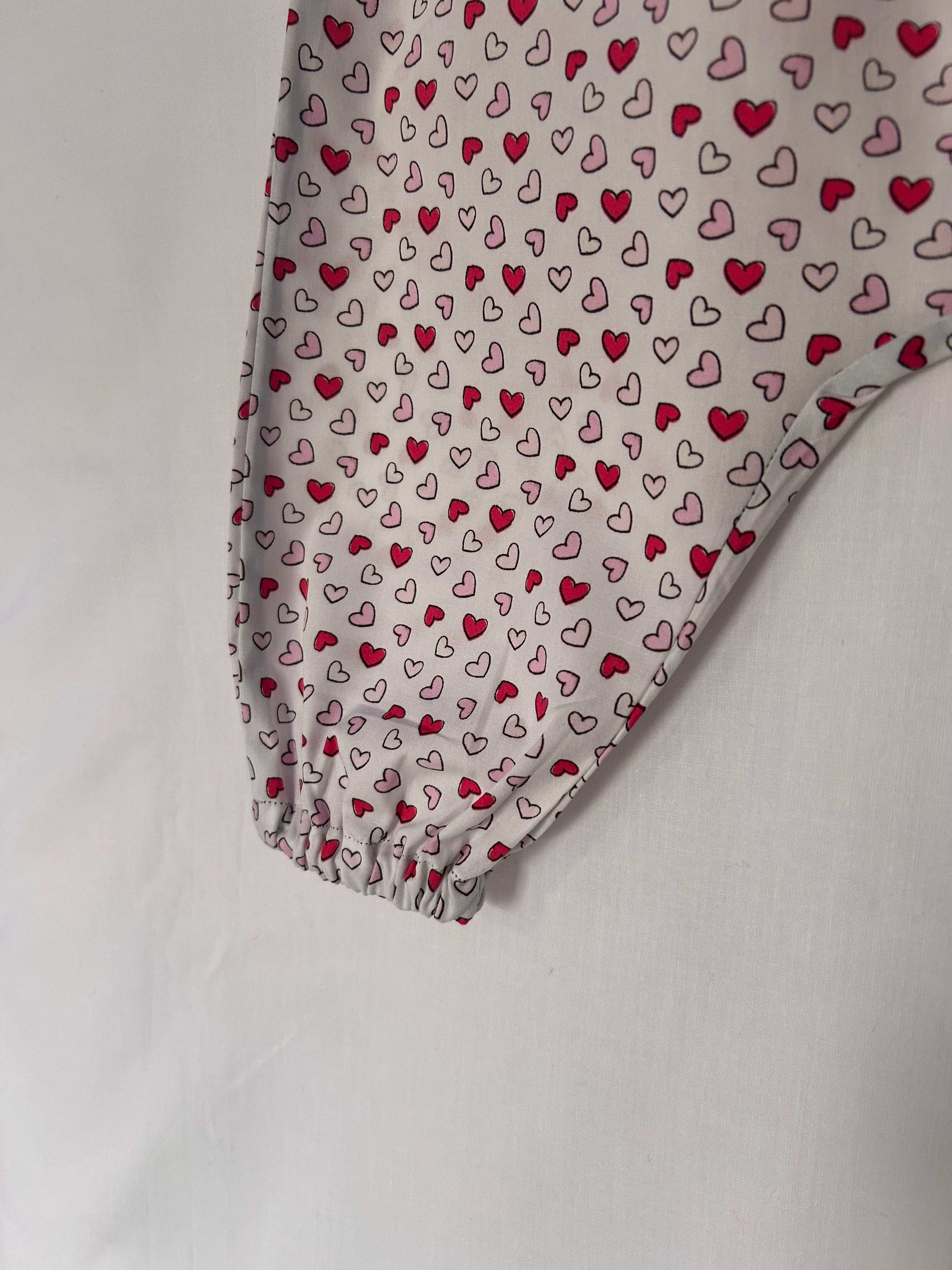 A young child wearing a handmade heart print romper. The romper has a bold heart print on soft, lightweight fabric. It has thin, shoulder straps and ruched neckline, relaxed, comfortable fit.