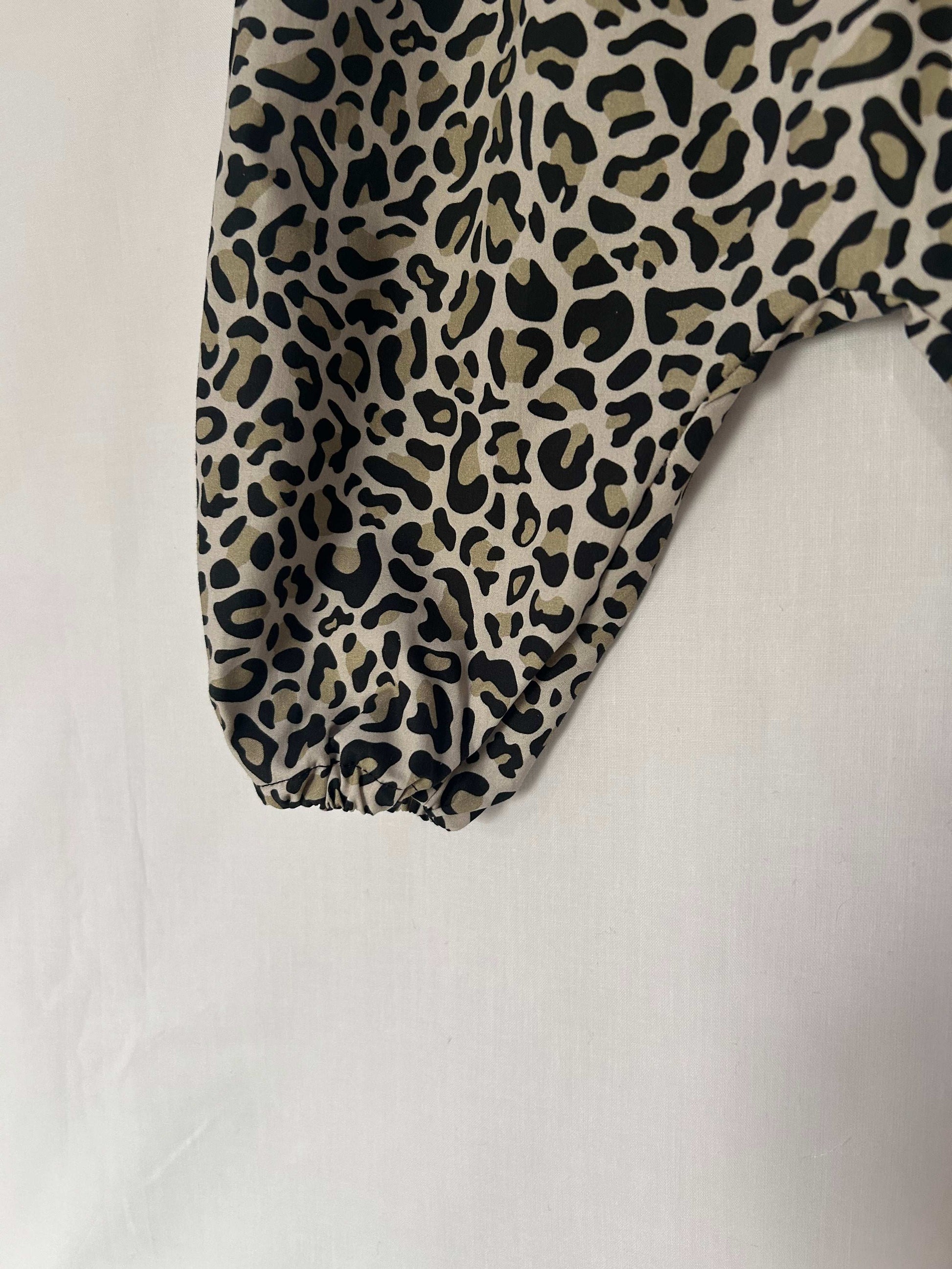 A young child wearing a handmade animal romper. The romper has a monochrome leopard print on soft, lightweight fabric. It has thin, shoulder straps and ruched neckline, relaxed, comfortable fit.