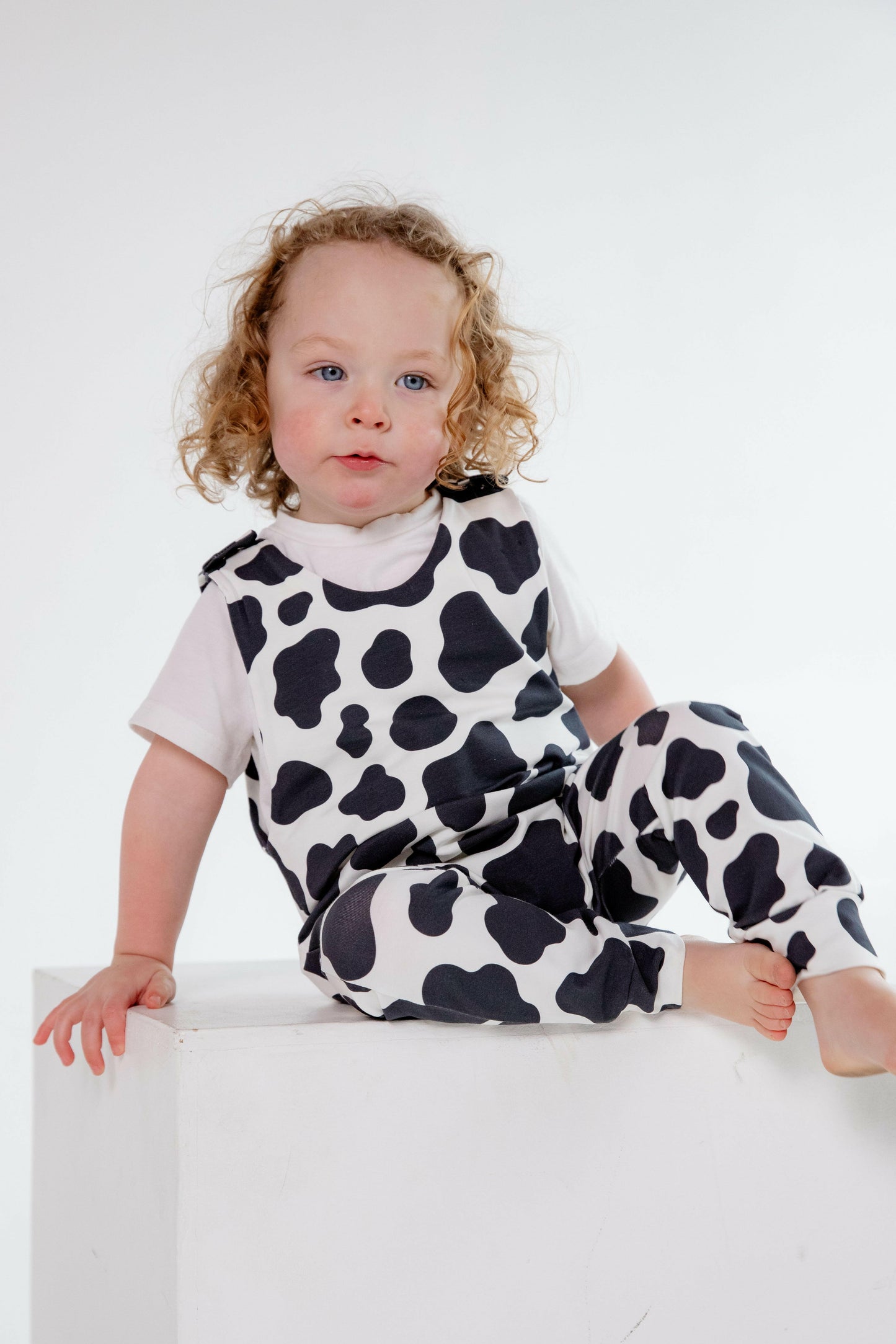 Cow animal print romper handmade for babies and toddlers, fun for running, jumping and climbing. Dungarees style outfit in a stretchy cotton fabric handmade in Oxfordshire.
