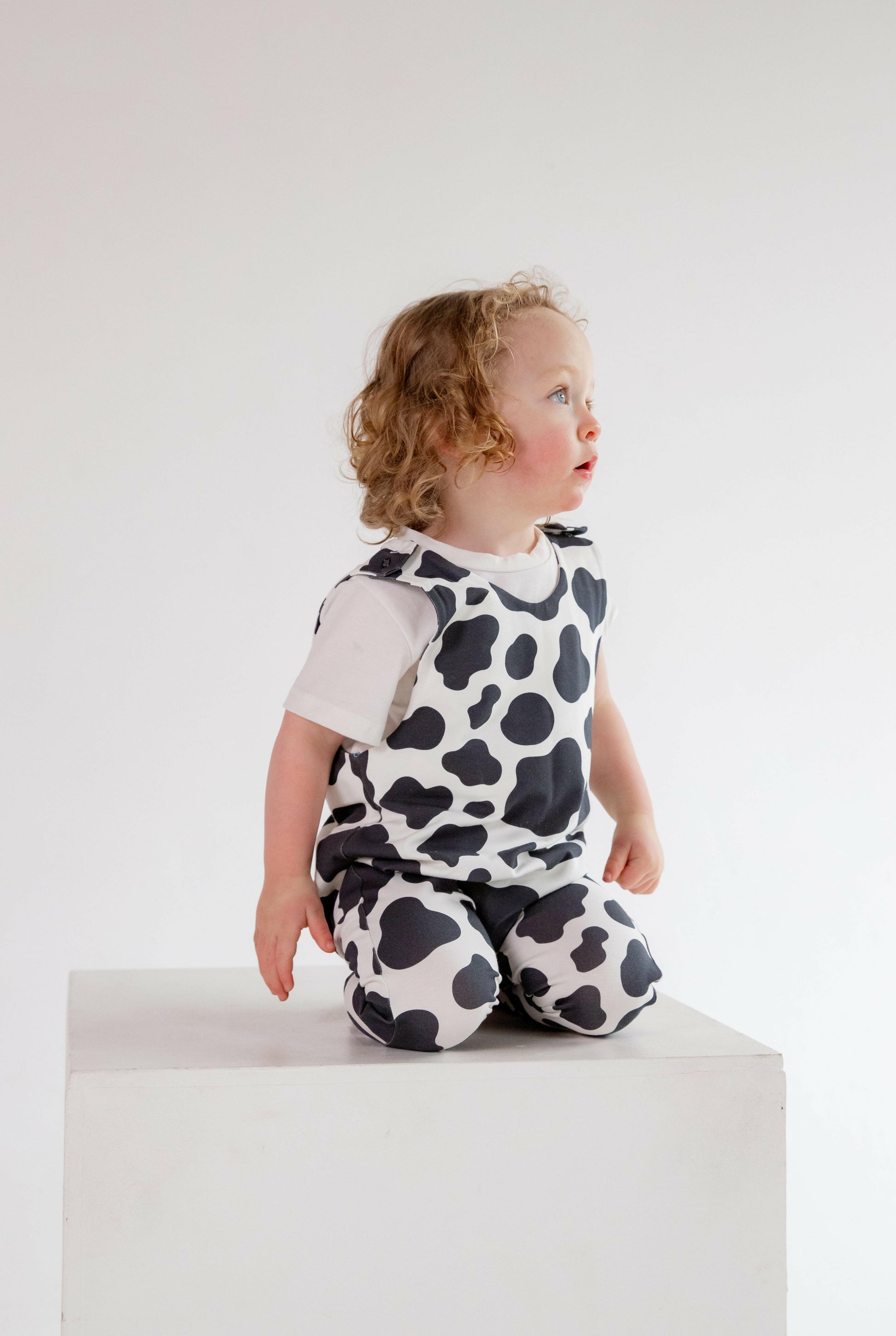 Cow animal print romper handmade for babies and toddlers, fun for running, jumping and climbing. Dungarees style outfit in a stretchy cotton fabric handmade in Oxfordshire.