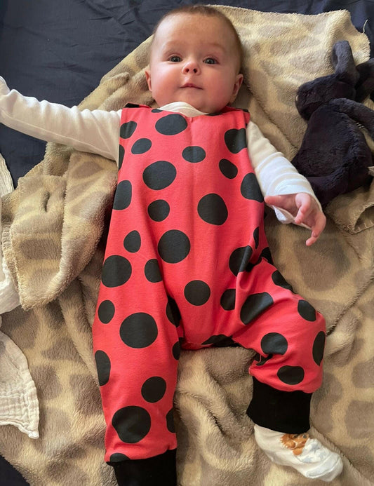 Red and black ladybird print romper handmade for babies and toddlers, fun for running, jumping and climbing. Dungarees style outfit in a stretchy cotton fabric handmade in Oxfordshire.