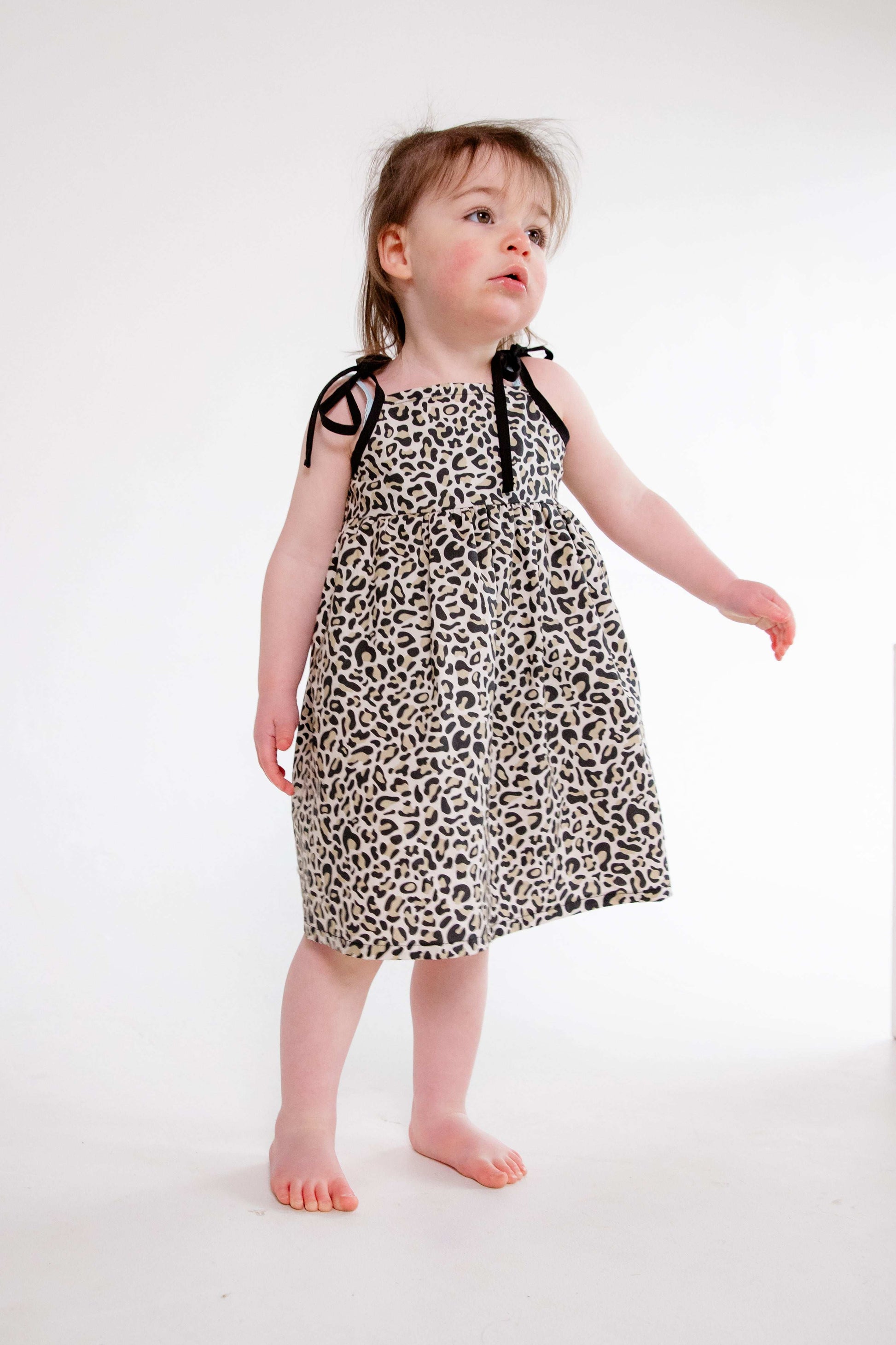 This handmade cotton dress features a bold leopard print, soft gathered skirt, and sweet bow-tie shoulder straps. Perfect for stylish little explorers with big personalities.