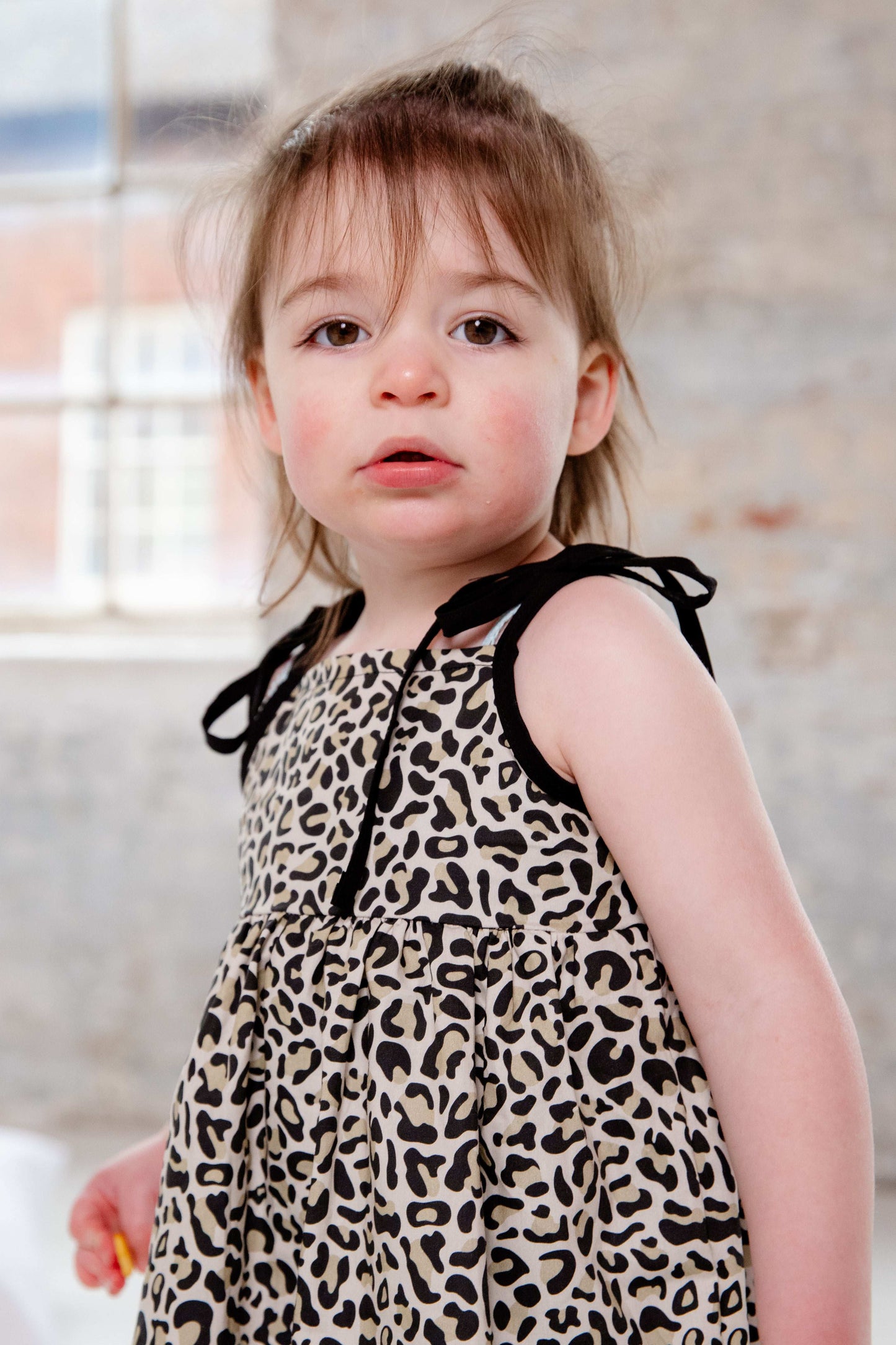 This handmade cotton dress features a bold leopard print, soft gathered skirt, and sweet bow-tie shoulder straps. Perfect for stylish little explorers with big personalities.