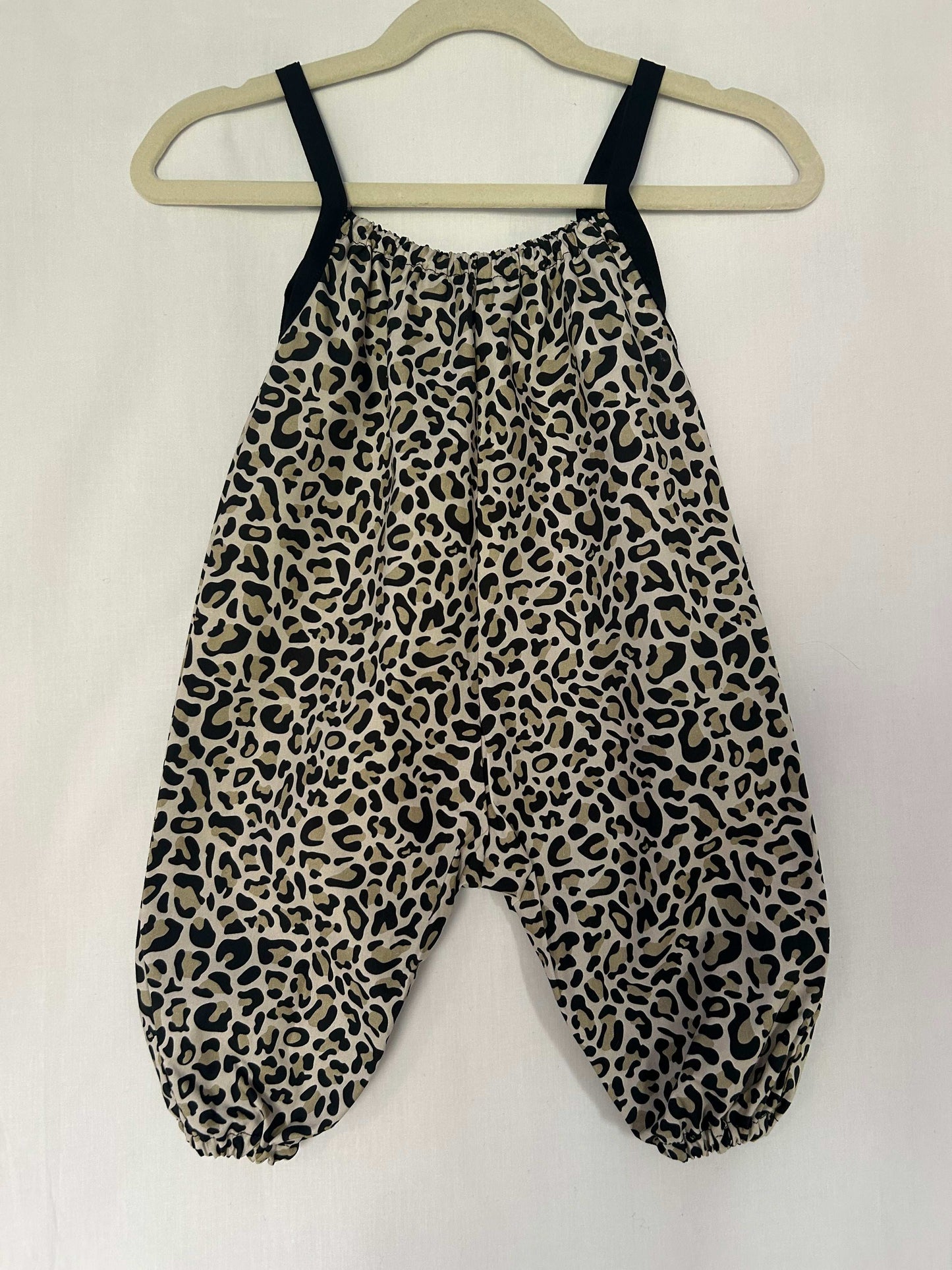 A young child wearing a handmade animal romper. The romper has a monochrome leopard print on soft, lightweight fabric. It has thin, shoulder straps and ruched neckline, relaxed, comfortable fit. 