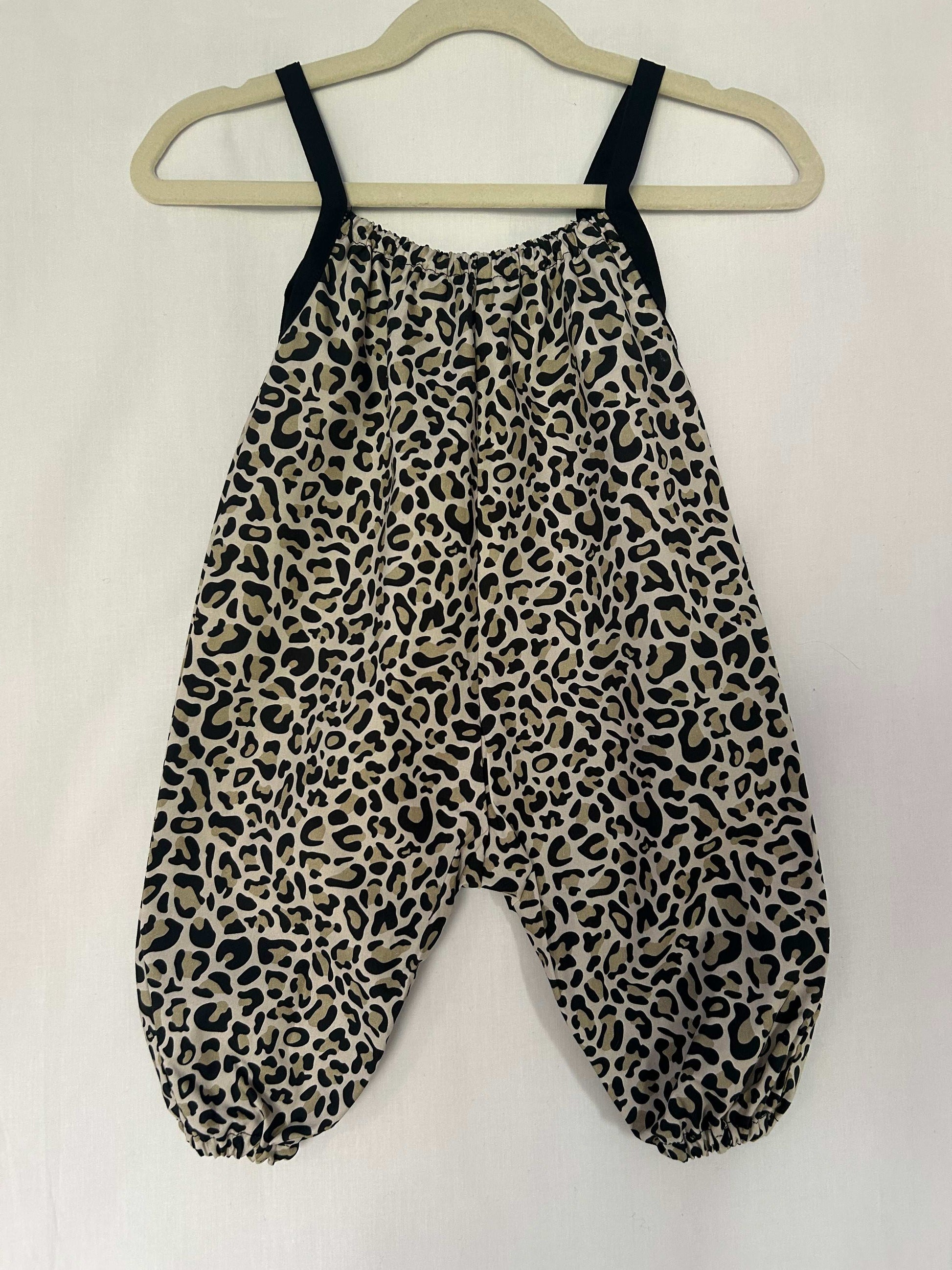 A young child wearing a handmade animal romper. The romper has a monochrome leopard print on soft, lightweight fabric. It has thin, shoulder straps and ruched neckline, relaxed, comfortable fit. 