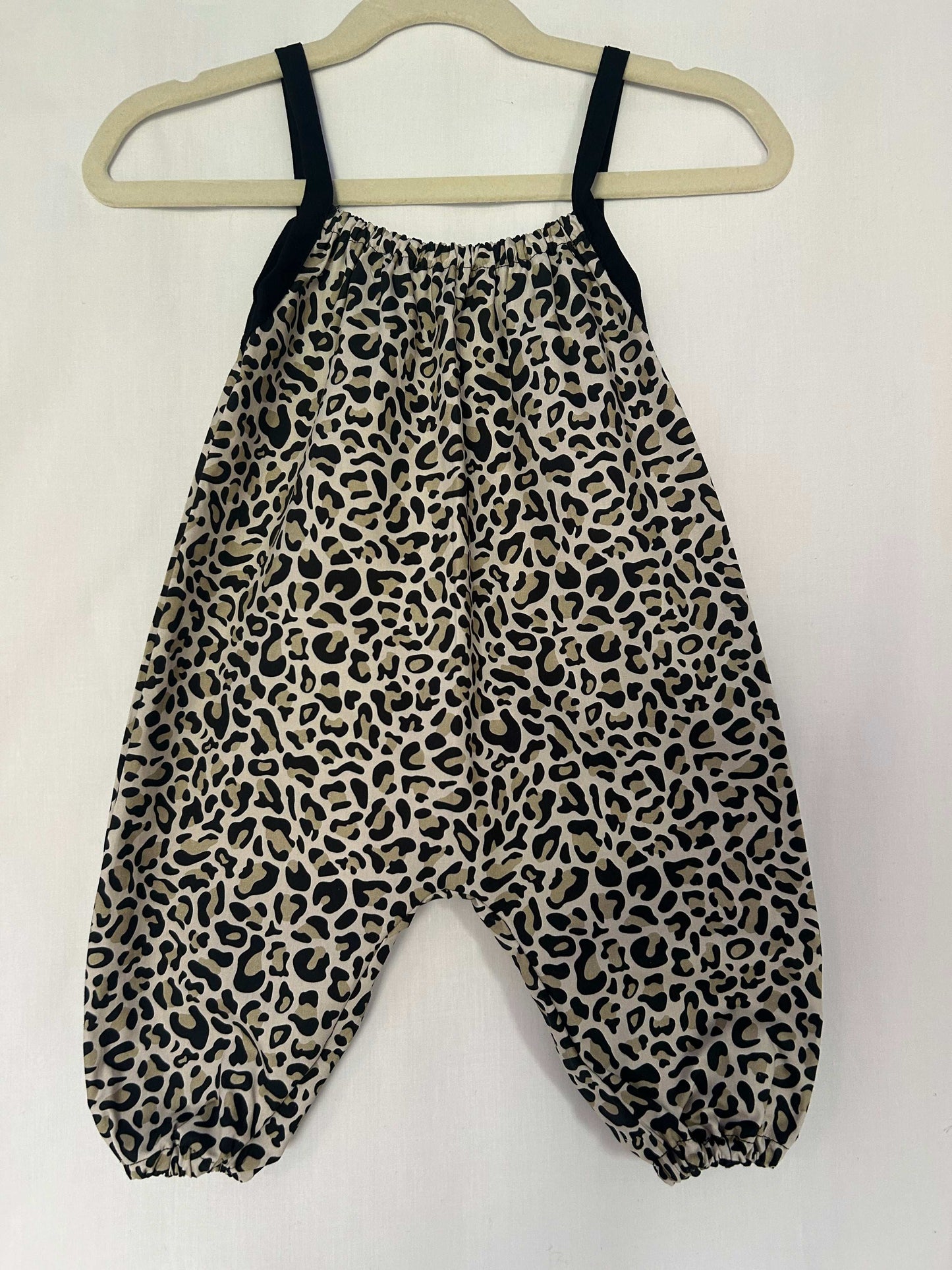 A young child wearing a handmade animal romper. The romper has a monochrome leopard print on soft, lightweight fabric. It has thin, shoulder straps and ruched neckline, relaxed, comfortable fit. 