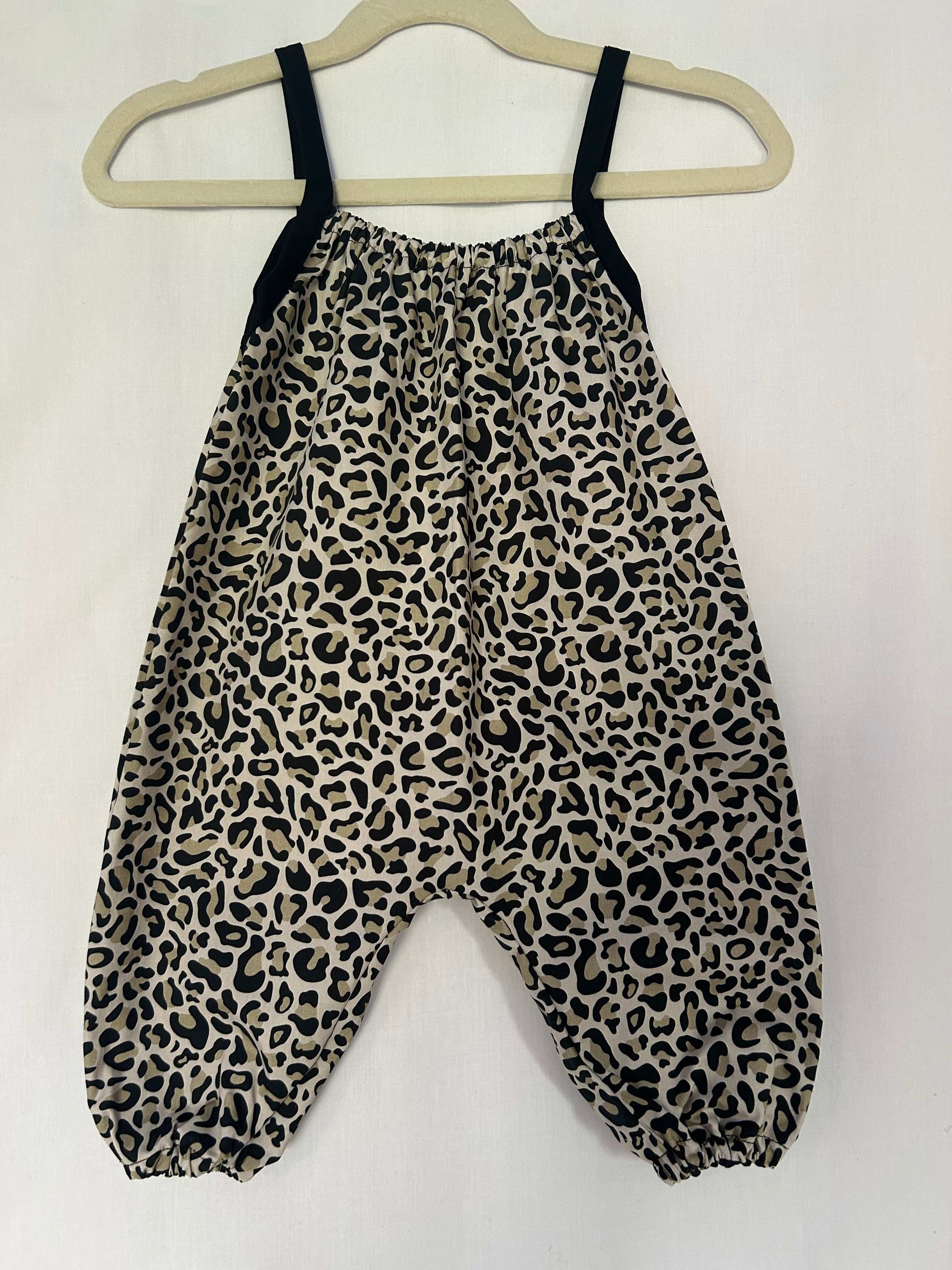 A young child wearing a handmade animal romper. The romper has a monochrome leopard print on soft, lightweight fabric. It has thin, shoulder straps and ruched neckline, relaxed, comfortable fit. 