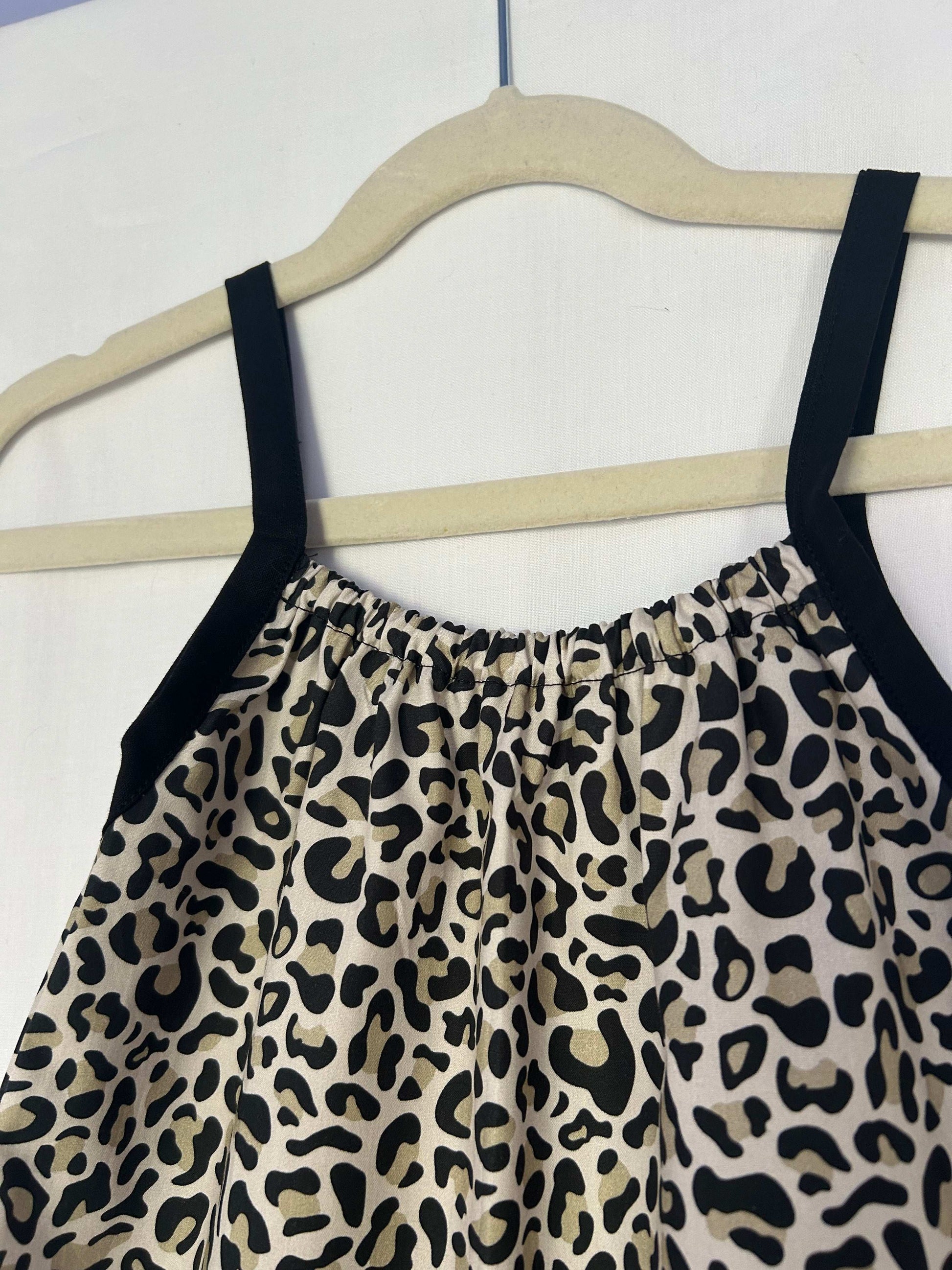 A young child wearing a handmade animal romper. The romper has a monochrome leopard print on soft, lightweight fabric. It has thin, shoulder straps and ruched neckline, relaxed, comfortable fit. 