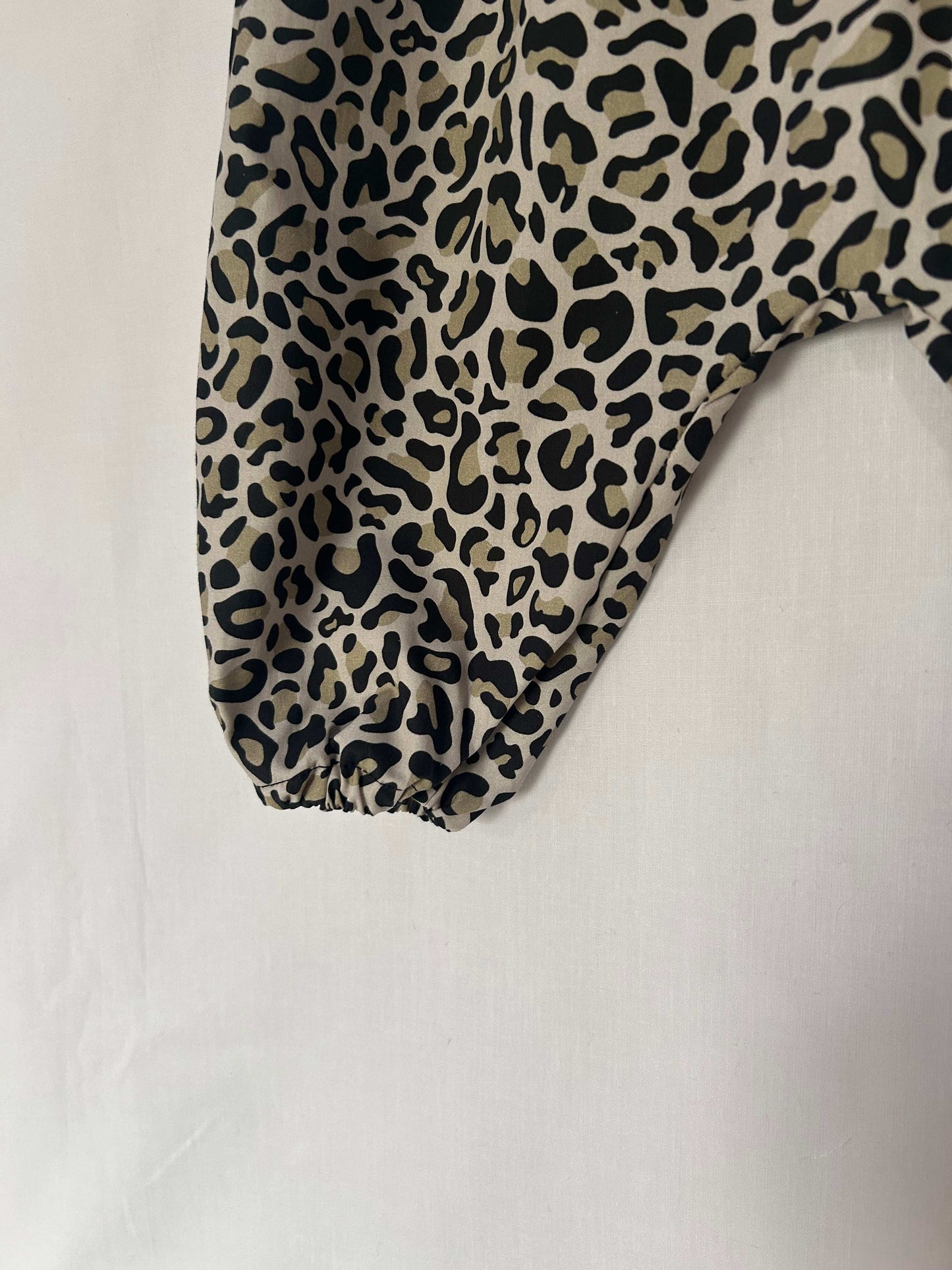 A young child wearing a handmade animal romper. The romper has a monochrome leopard print on soft, lightweight fabric. It has thin, shoulder straps and ruched neckline, relaxed, comfortable fit. 