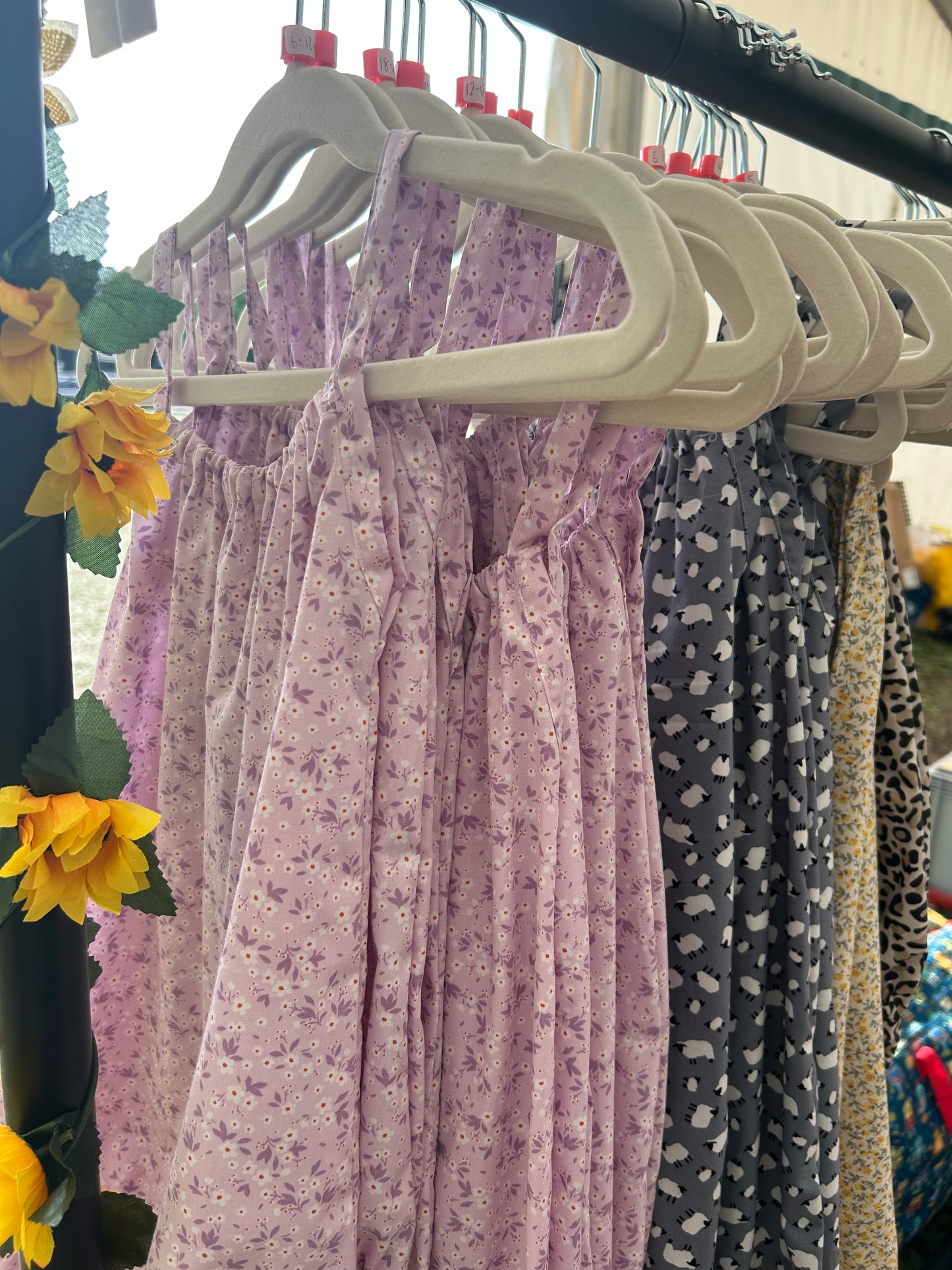 A young child wearing a handmade floral print romper. The romper has a lilac flower print on soft, lightweight fabric. It has thin, shoulder straps and ruched neckline, relaxed, comfortable fit. 